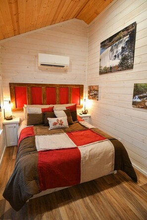 Ein Schlafzimmer mit Holzboden, einem Bett mit rotbrauner Bettwäsche, einem roten Kopfteil und einer Wandklimaanlage.