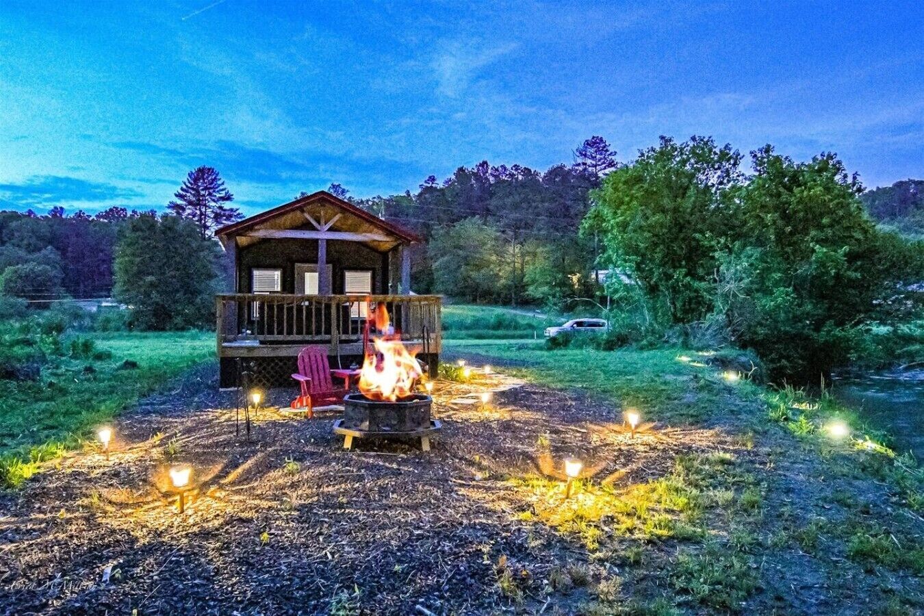 A cabin with a fire pit in the center, surrounded by outdoor lights, set in a forested area.