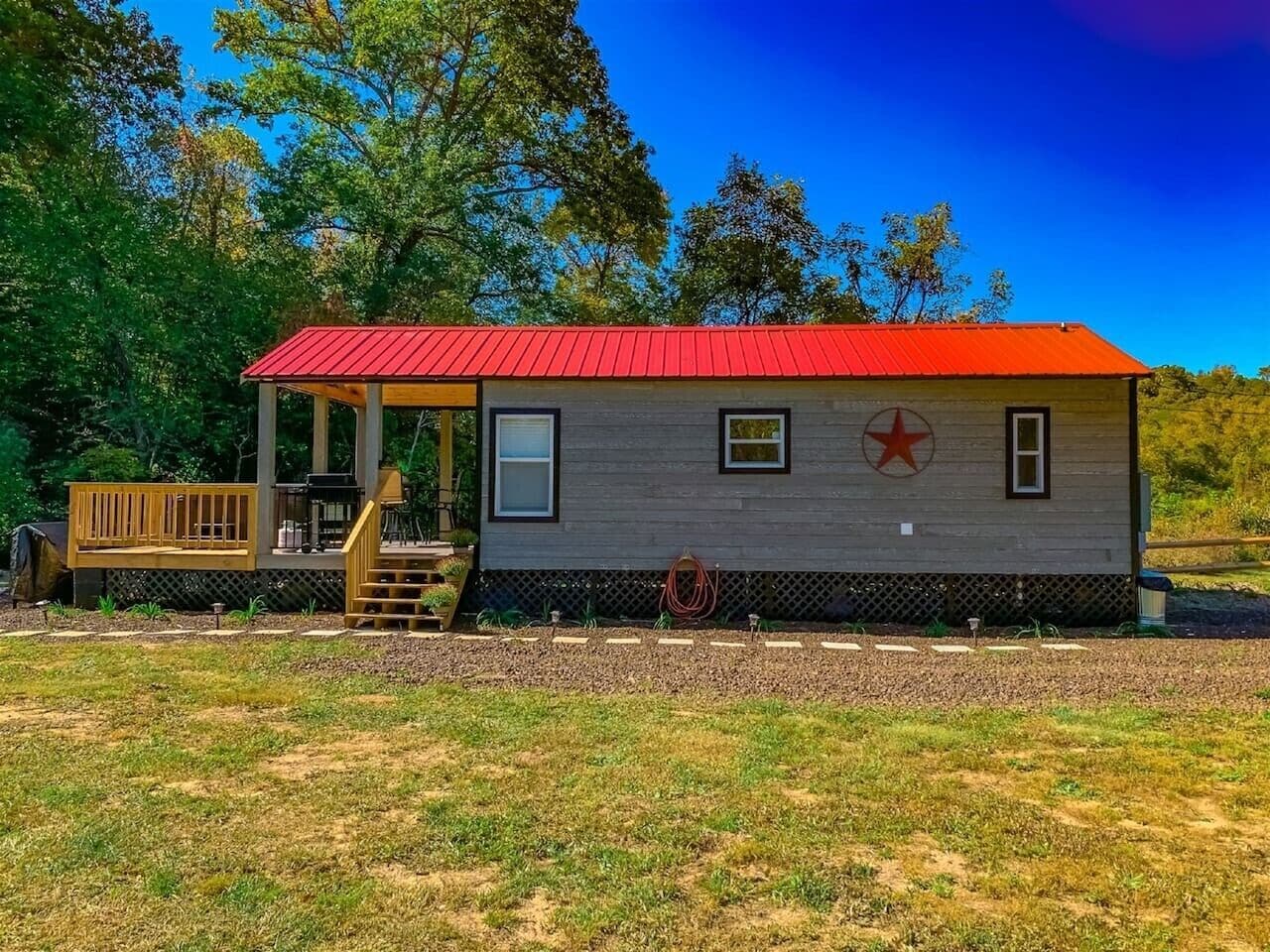 A small cabin with a red roof, a porch, and a wooden deck.