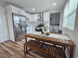 A modern kitchen with white cabinets, stainless steel appliances, and a wooden dining table. - Cozy 2-bedroom condo with AC in amazing Miami location (Miami)