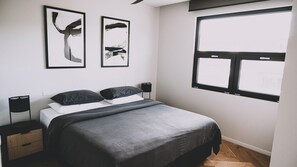 Une chambre à coucher avec un lit, deux œuvres d’art noir accrochées au mur, une fenêtre et une table de chevet avec une lampe.