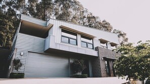 Une maison moderne à deux étages, dotée d’un toit plat, de grandes fenêtres et d’un garage.