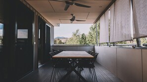Un espace extérieur abrité, aménagé pour les repas, avec une table et des chaises, un ventilateur de plafond et une vue sur l’extérieur.