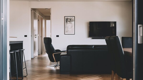 Un salon moderne avec un canapé en cuir noir, un fauteuil en cuir noir et un téléviseur à écran plat fixé au mur.