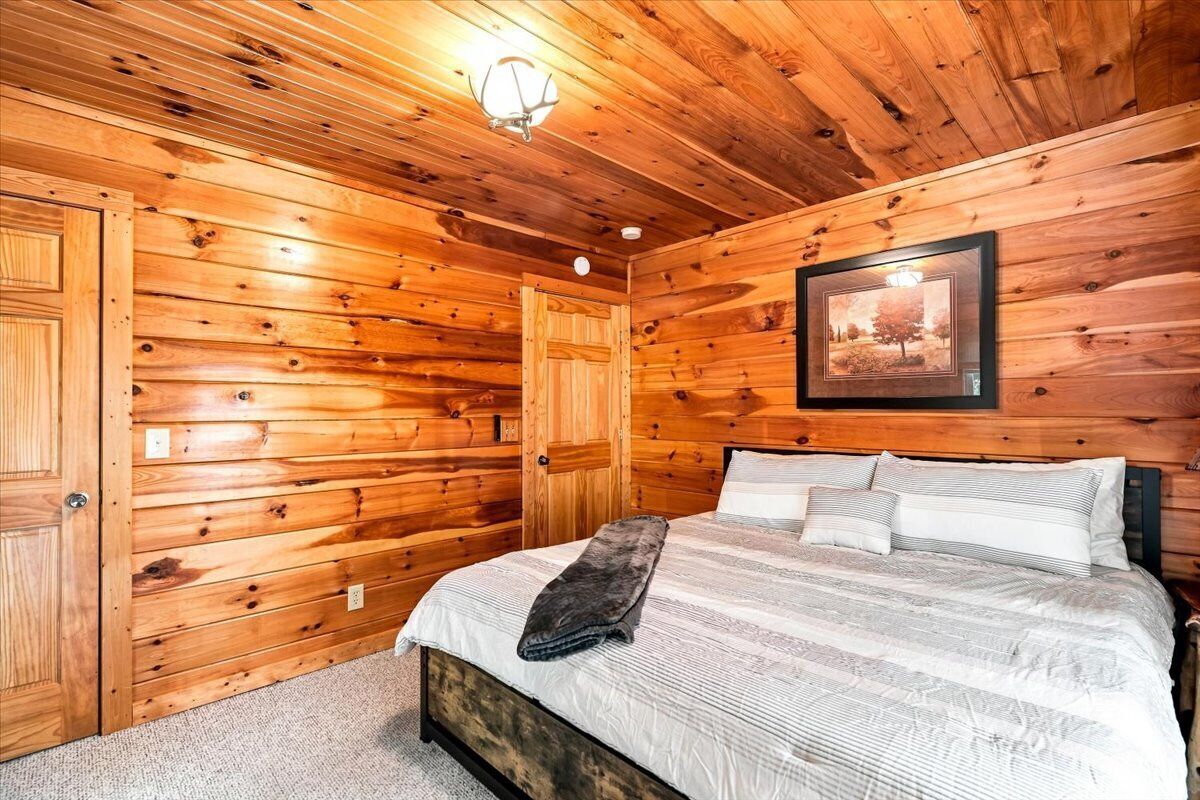 A wooden-paneled bedroom with a bed, a framed picture on the wall, and a door.