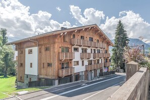 Un edificio de madera de varios pisos con balcones, una calle pavimentada al frente y montañas al fondo.