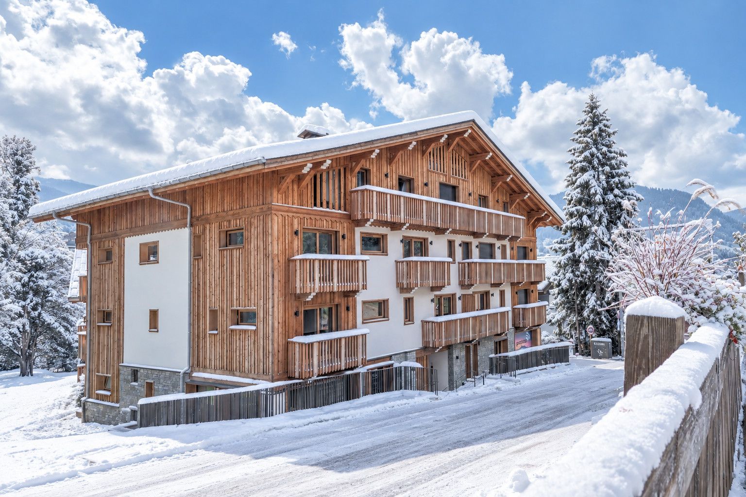 Una cabaña de madera de varios pisos con balcones, rodeada de árboles y montañas nevadas.