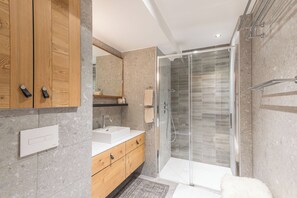 Un baño moderno con cabina de ducha de vidrio, muebles de madera y un lavamanos blanco.