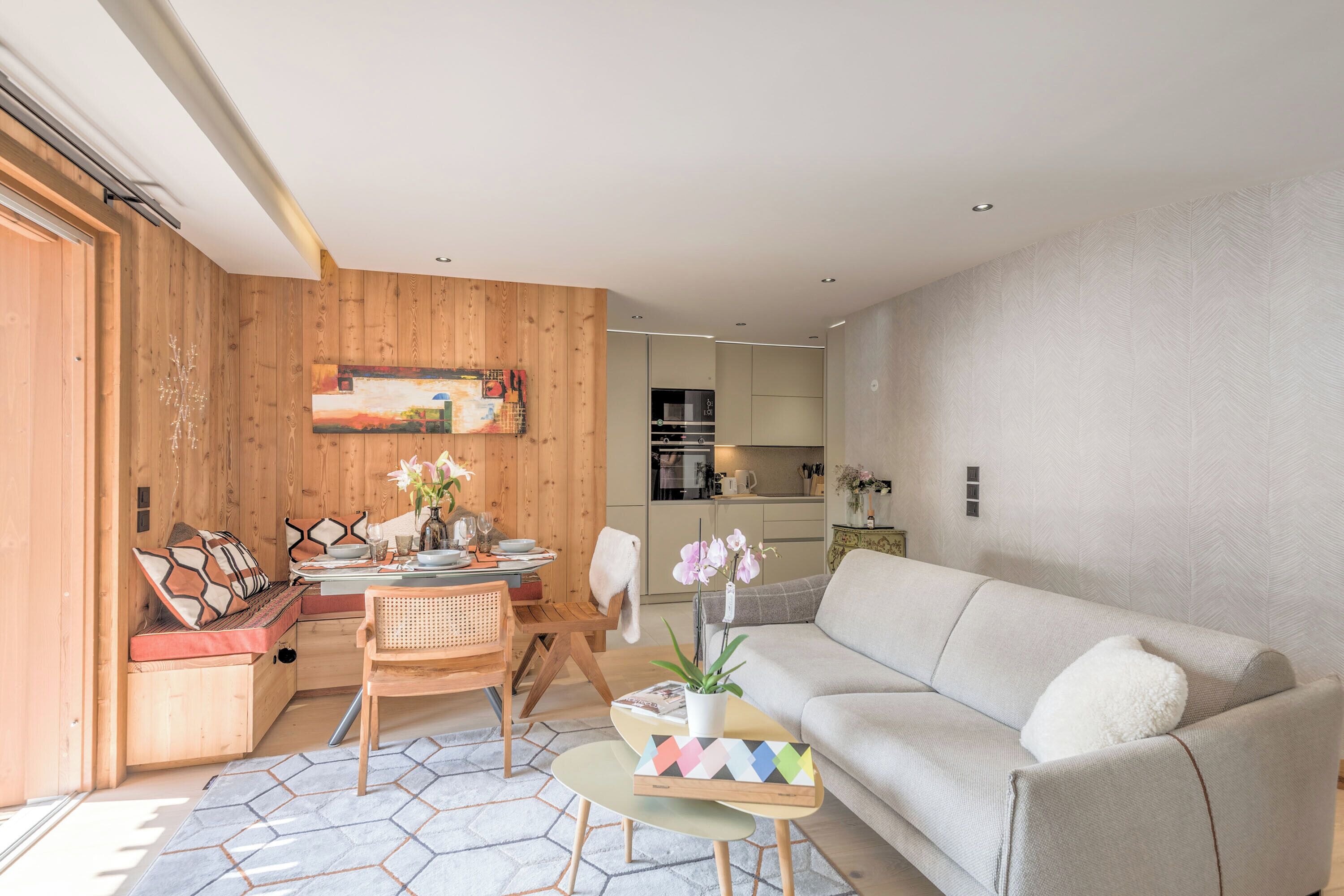 A modern living room with a sofa, dining table, and chairs. There is a kitchen in the background.