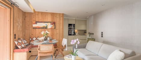 A modern living room with a sofa, dining table, and chairs. There is a kitchen in the background.