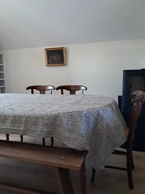 Una mesa de comedor con mantel estampado, dos sillas, un banco, un televisor y un cuadro en la pared.