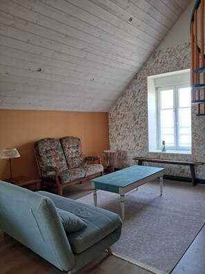 Una sala de estar acogedora con techo inclinado, un sofá, una mesa de centro y una ventana con cortinas.