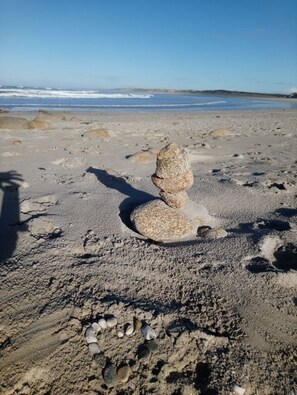 Ein Sandstrand mit einem Felsensturz im Vordergrund und dem Meer im Hintergrund.