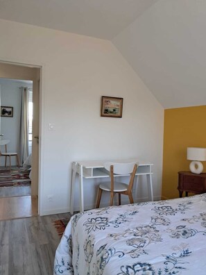 Een slaapkamer met een bed, een bureau met stoel, een schilderij aan de muur en een lamp op een nachtkastje.