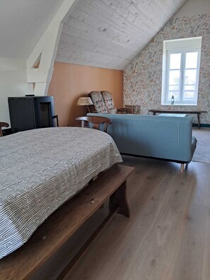 Ein Schlafzimmer mit einem Bett, einem Sessel, einem kleinen Tisch, einer Lampe und einem Fenster.