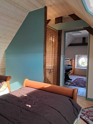 Un dormitorio con techo inclinado, una cama, un piano y vistas a un balcón.