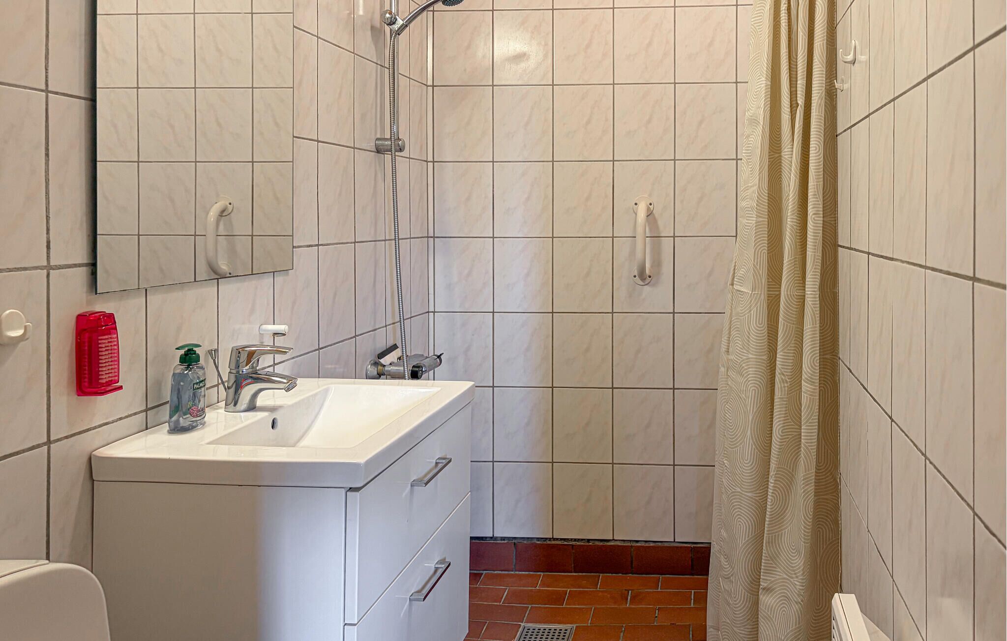 Un bagno con lavandino bianco, uno specchio, una doccia con soffione manuale e un tenda da doccia fantasia.