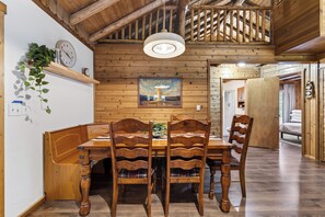 A wooden dining area with a table and chairs, a clock, and a framed picture on the wall.