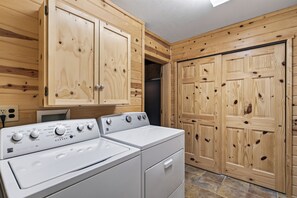 Ein Waschbereich mit einer Frontlademaschine und einem Trockner, Holzschränken und einer großen Holztür.