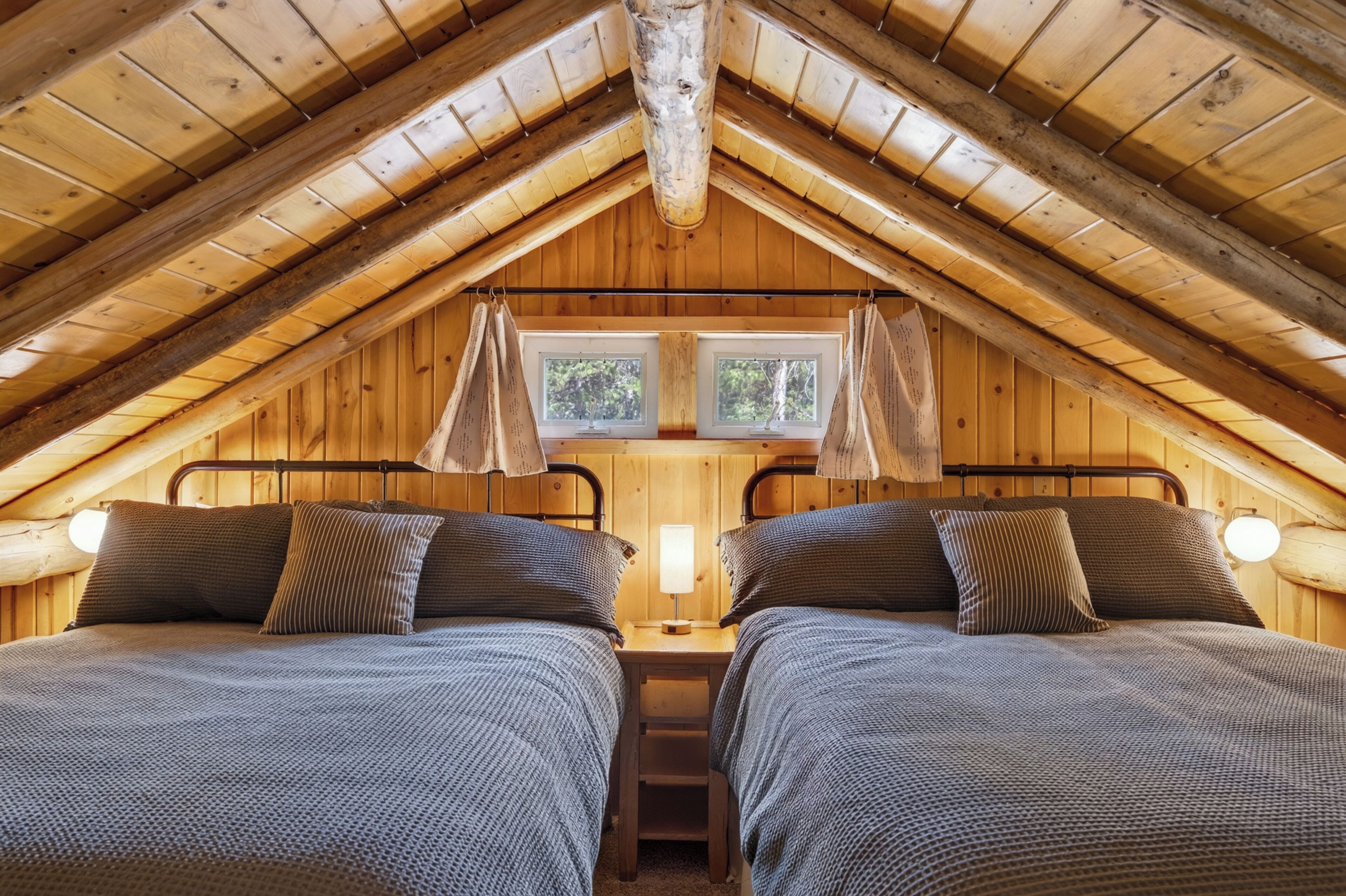 Un dormitorio acogedor en el ático con dos camas, vigas de madera y una ventana.