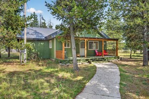 A small cabin with a porch, a pathway leading to it, and a surrounding wooded area.