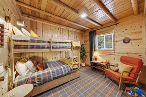 A wooden cabin interior with bunk beds, a small table, a chair, and a window with curtains.