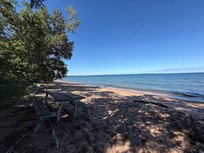 A beach with a picnic table and a tree providing shade. - Crane Cabin-Set directly along the sandy shores of Amnicon Bay, Aajijash (La Pointe)