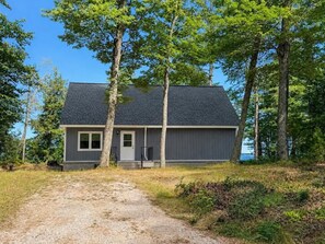 A single-story house with a dark roof, a front door, and a small porch. - Crane Cabin-Set directly along the sandy shores of Amnicon Bay, Aajijash (La Pointe)