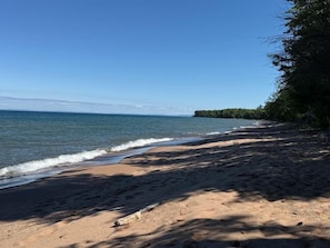 A beach with clear skies, calm water, and a distant landmass. - Crane Cabin-Set directly along the sandy shores of Amnicon Bay, Aajijash (La Pointe)