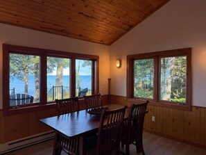 A dining area with a wooden table and chairs, large windows with a view of trees and a body of water. - Crane Cabin-Set directly along the sandy shores of Amnicon Bay, Aajijash (La Pointe)