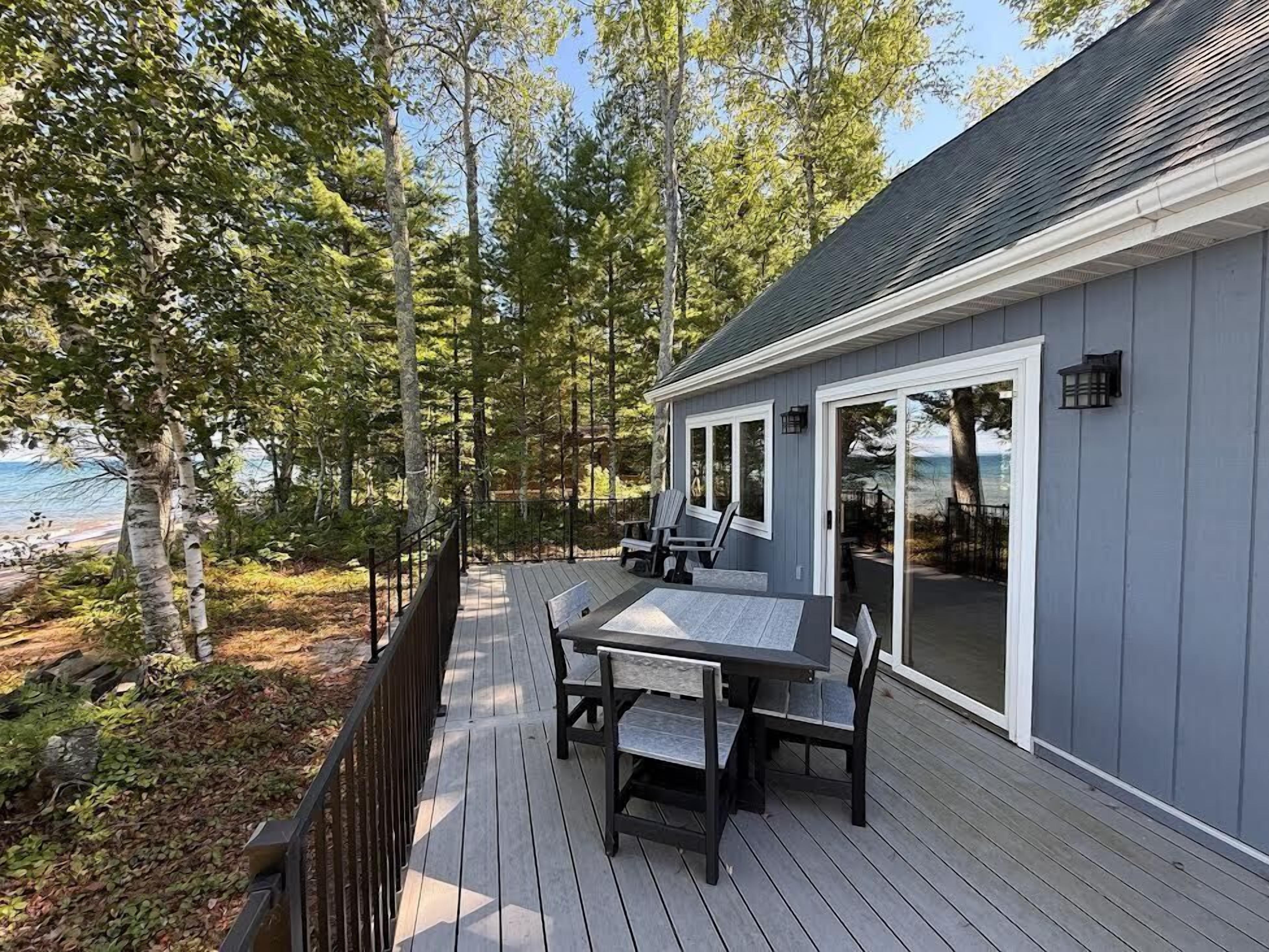 A deck with a table and chairs, overlooking a beach and trees.