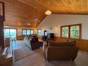 A spacious living room with a high ceiling, wooden flooring, and large windows. - Crane Cabin-Set directly along the sandy shores of Amnicon Bay, Aajijash (La Pointe)