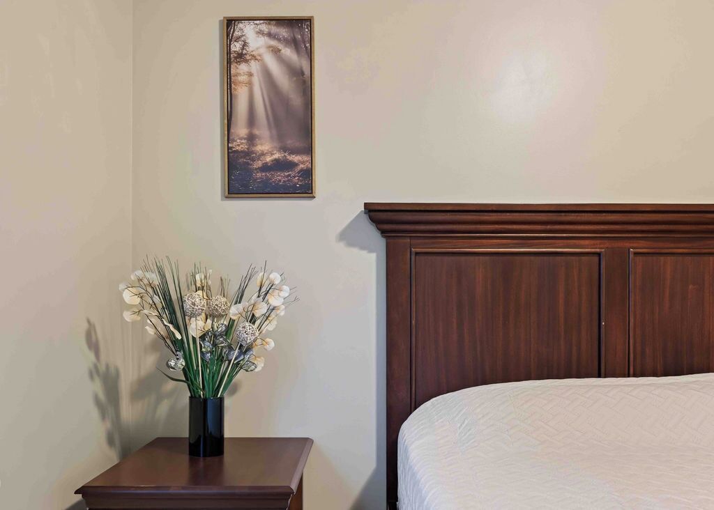 Un dormitorio con cabecera de madera, una mesita de noche con un florero y un cuadro en la pared.