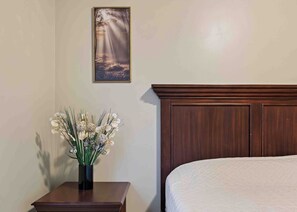 A bedroom with a wooden headboard, a bedside table with a vase of flowers, and a framed picture on the wall.