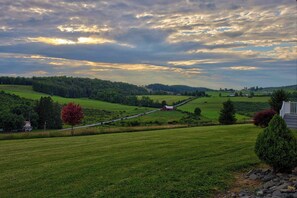 A rural landscape with rolling hills, a red barn, and a house with a white exterior.