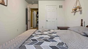 Un dormitorio con cama, mesita de noche, lámpara colgante y una puerta que da a otra habitación.