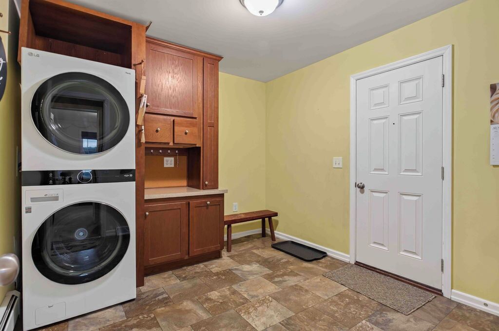 A laundry room with two front-loading washing machines, wooden cabinets, a bench, and a white door.
