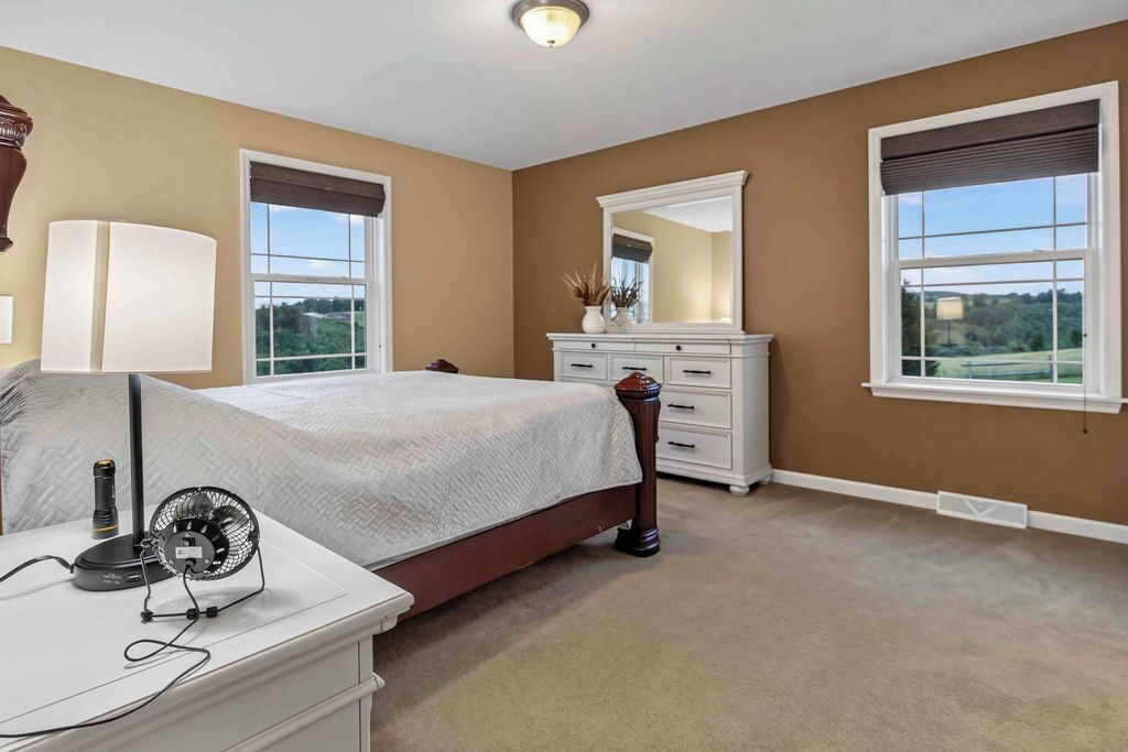 A bedroom with a bed, bedside table, lamp, dresser, mirror, and windows.