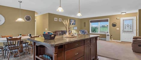 A kitchen with a central island, wooden cabinetry, pendant lighting, and a dining area with chairs and a table.