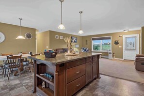 A kitchen with a central island, wooden cabinetry, pendant lighting, and a dining area with chairs and a table.