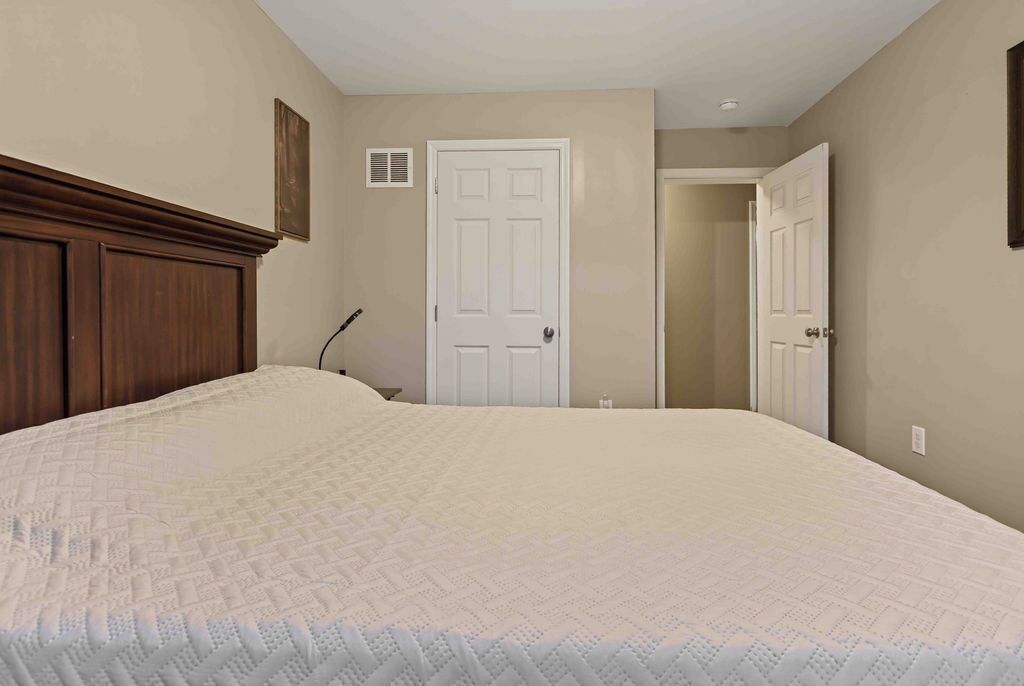 Un dormitorio con una cama grande, cabecera de madera, una puerta blanca y un ventanal pequeño.