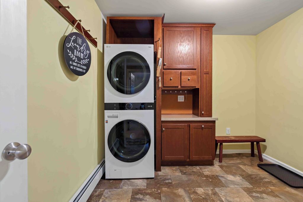 A laundry room with two washing machines, wooden cabinets, and a bench.