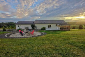 A house with a covered porch, a lawn, and a fire pit area with chairs.