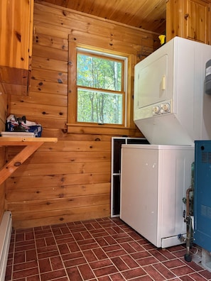 A compact laundry room with wooden walls, a window, and a white washing machine.