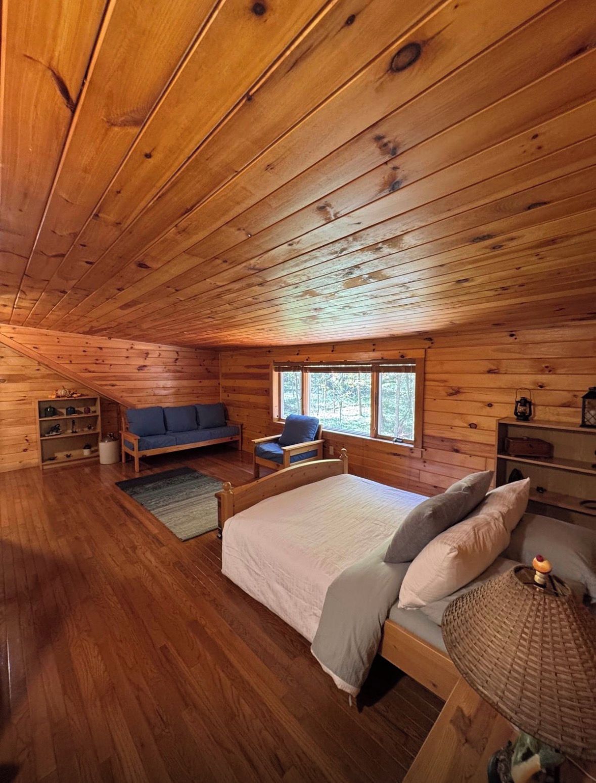 Een vakantiehuisje met houten balkenplafond, een bed met kussens, een bank en een stoel.