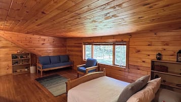 Een vakantiehuisje met houten balkenplafond, een bed met kussens, een bank en een stoel.