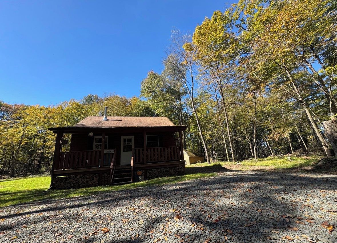 A cabin with a stone foundation, a wooden deck, and a gravel driveway.