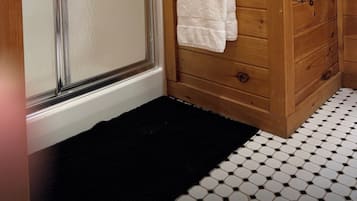 A wooden interior with a glass door leading to a shower area, a white towel hanging on a rack, and a black mat at the entrance.