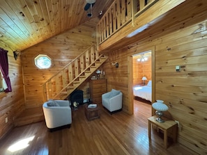 A wooden cabin interior with a staircase, a fireplace, two sofas, and a bed.