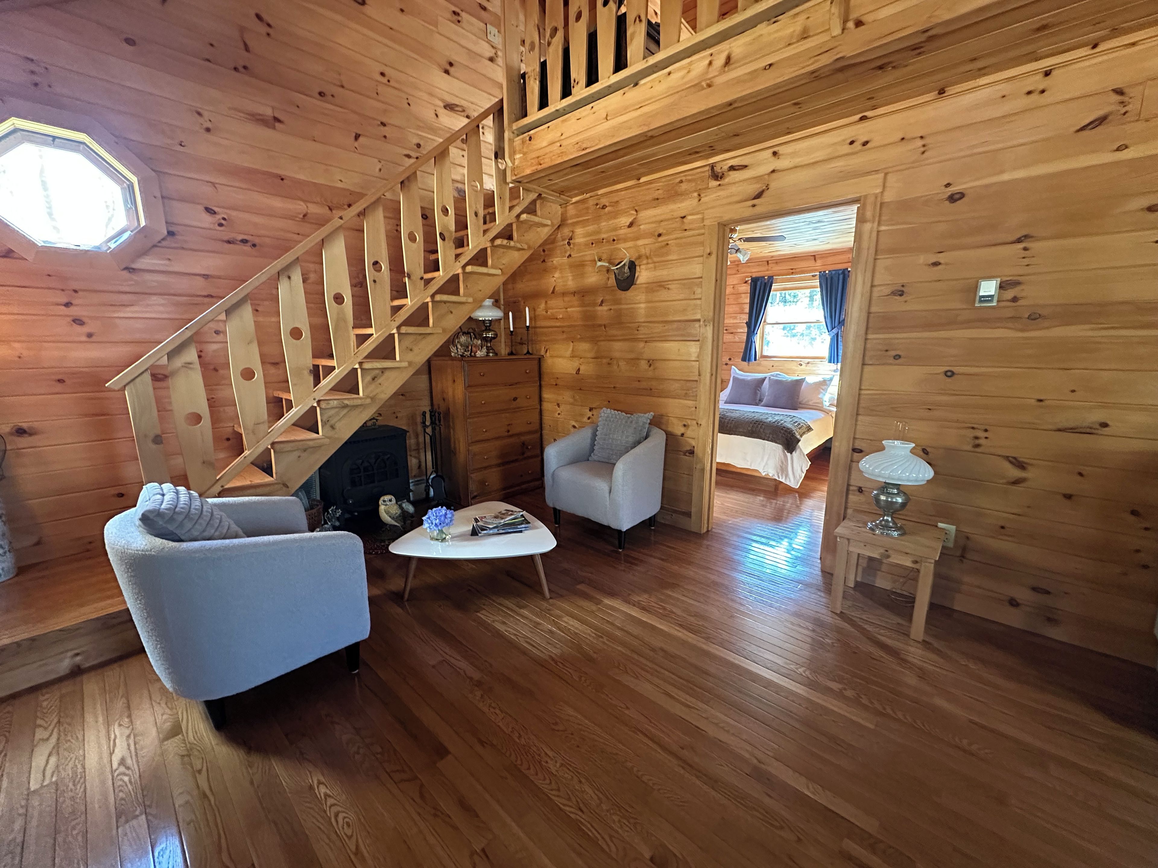 A wooden interior with a staircase, a fireplace, two sofas, a coffee table, and a bed.